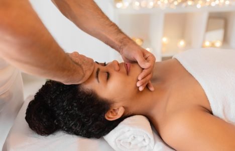 Therapeutic face massage in a serene spa A skilled masseur provides a relaxing face massage to a client African American lady in a tranquil spa setting with dim lighting and candles